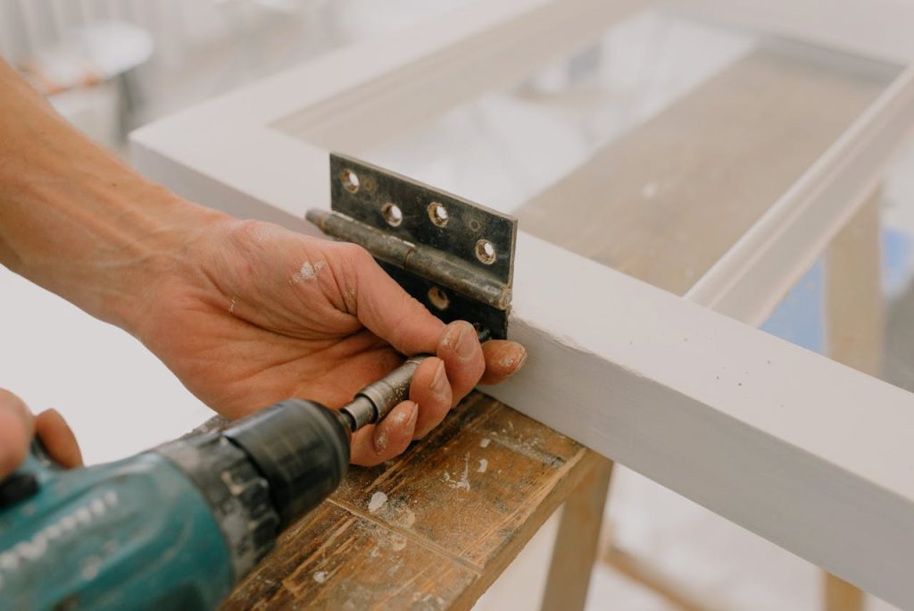 crop-workman-drilling-hinge-on-window-frame-5691518 Crop unrecognizable worker drilling metal hinge on white window frame during house renovation